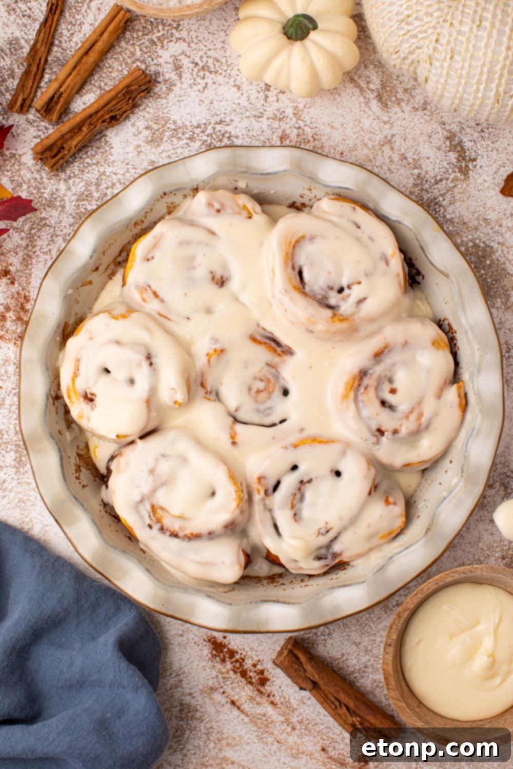 Effortless 2-Ingredient Pumpkin Cinnamon Rolls No Yeast 24 looking down to a marbled counter with cinnamon sticks, pumpkins and more around a pie plate full of pumpkin cinnamon rolls that are glazed