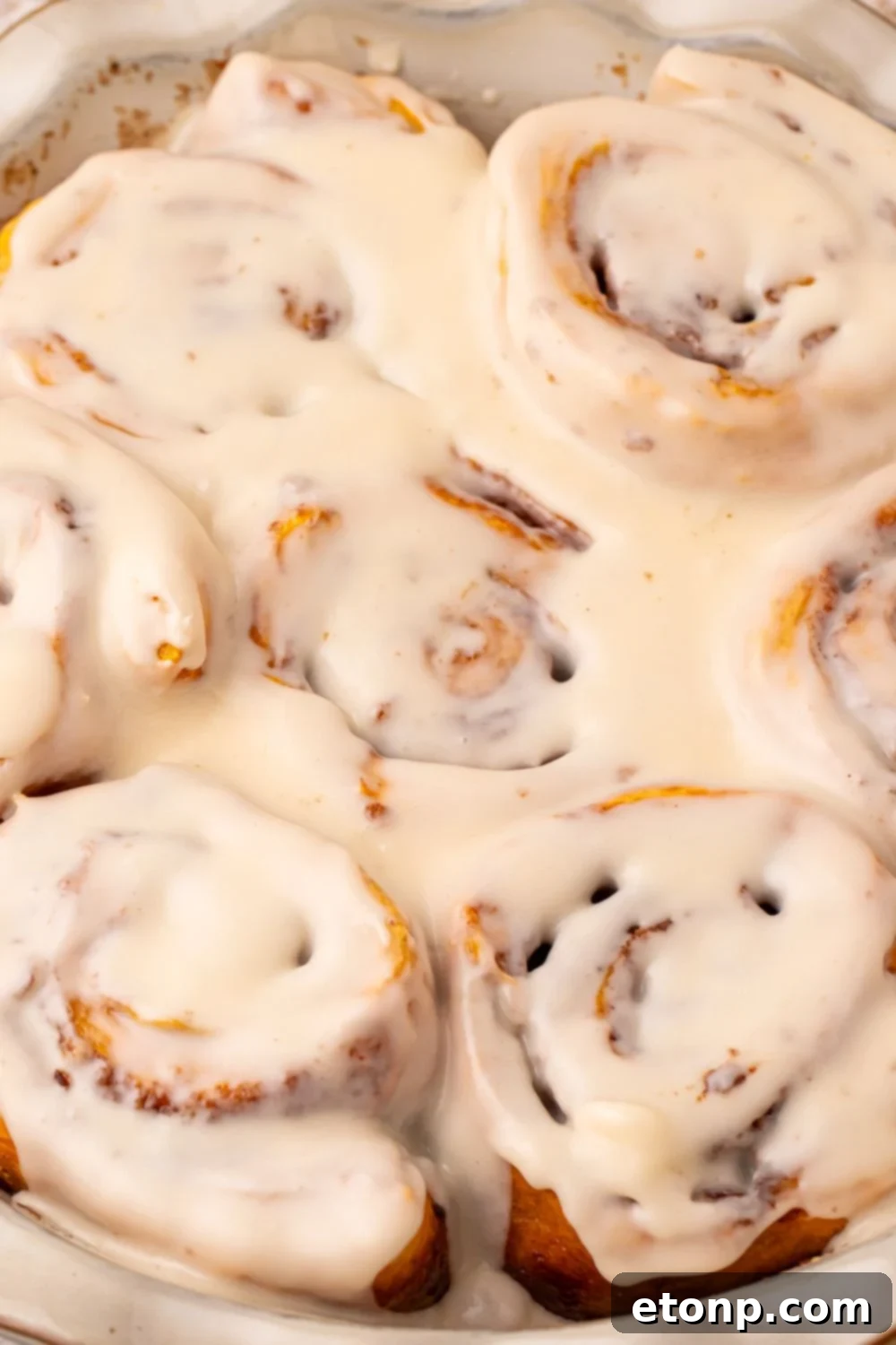 Effortless 2-Ingredient Pumpkin Cinnamon Rolls No Yeast 28 view of a close up of Pumpkin Cinnamon Rolls in a pan on table. You can see all the glaze seeped into the rolls