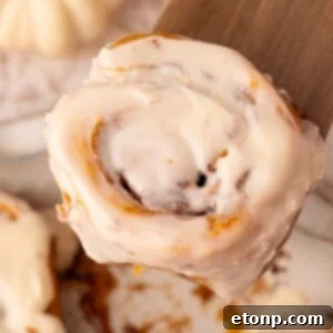 Effortless 2-Ingredient Pumpkin Cinnamon Rolls No Yeast 29 2 Ingredient Pumpkin Cinnamon Rolls in a pan with one on a wooden spatula being lifted above the pan