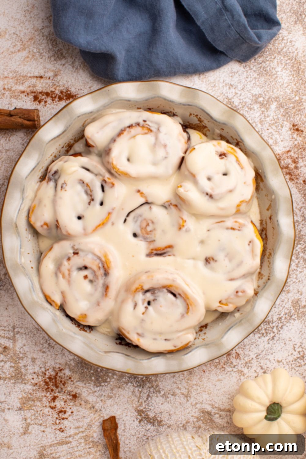 Effortless 2-Ingredient Pumpkin Cinnamon Rolls No Yeast 4 Pumpkin Cinnamon Rolls in a round dish on table with cinnamon sticks and tiny pumpkins around the table to have a fall vibe