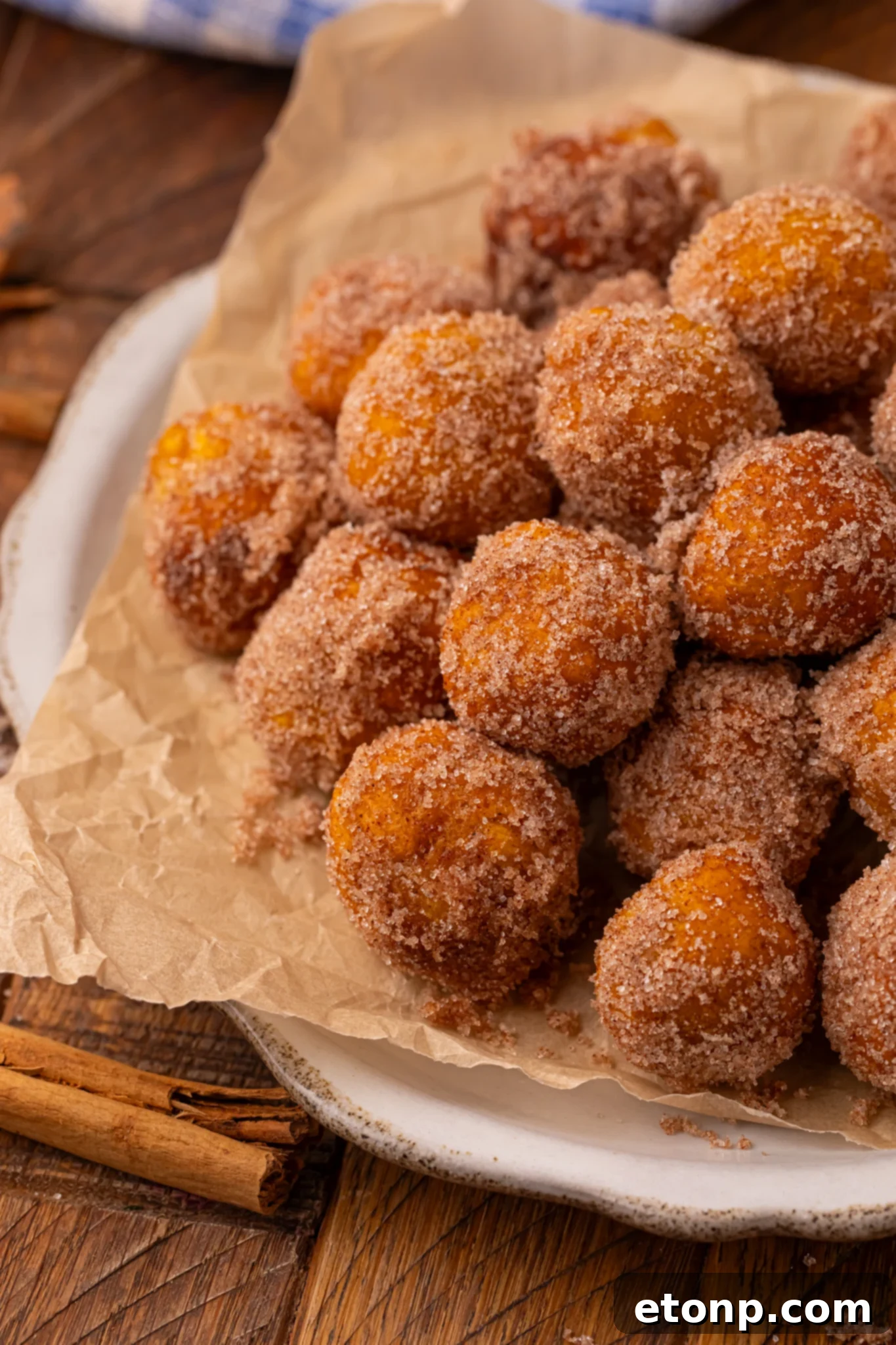 Effortless Two-Ingredient Pumpkin Pie Bites 2 Up close shot of a pile of Pumpkin Pie Donut Holes stacked on a parchment lined white platter on a wooden table.