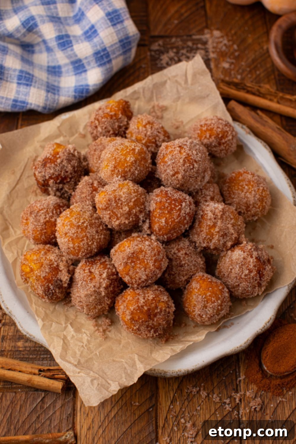 Effortless Two-Ingredient Pumpkin Pie Bites 13 Pumpkin Pie Donut Holes on a platter with a parchment paper lined platter on a wooden table with cinnamon sticks around table and a towel