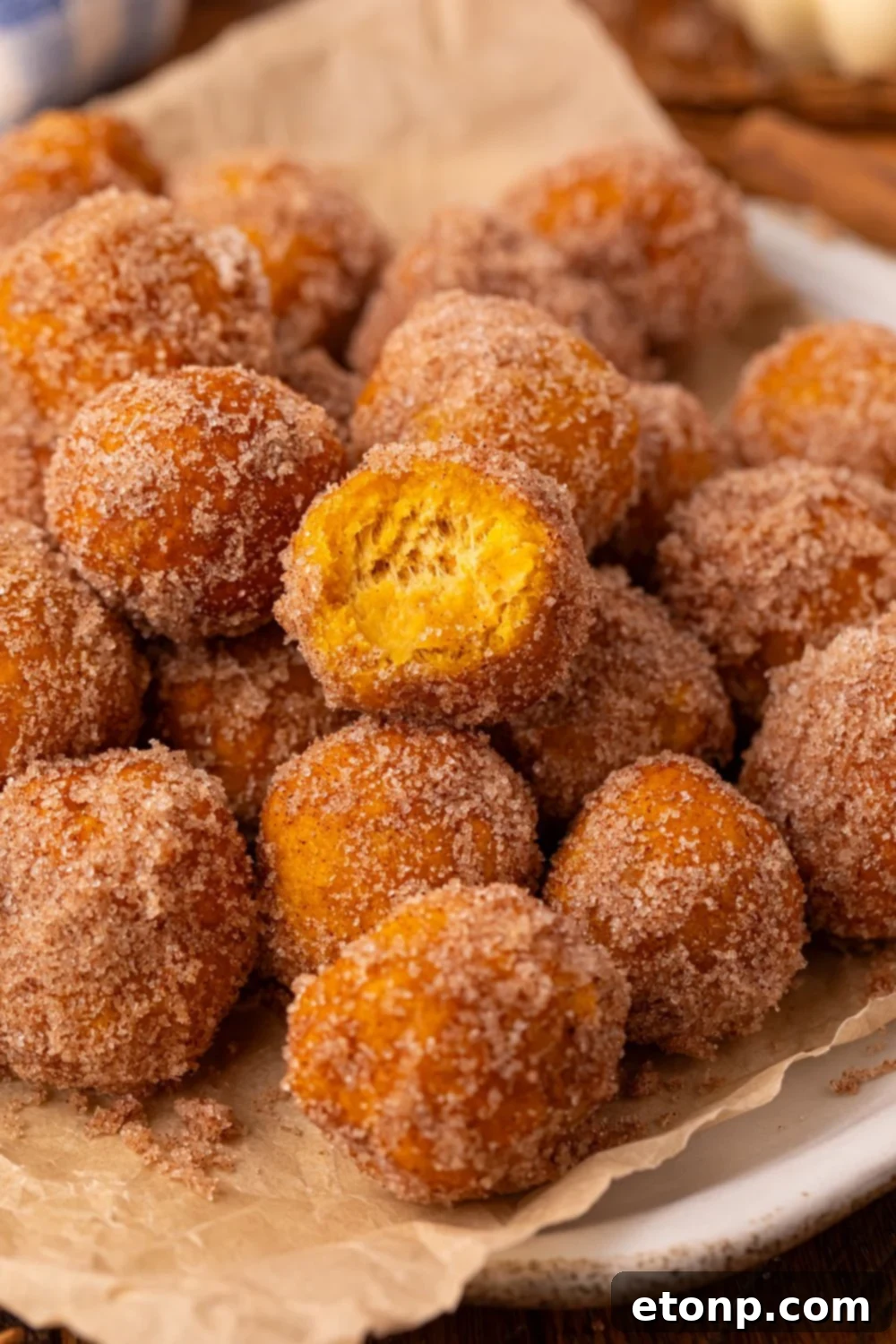 Effortless Two-Ingredient Pumpkin Pie Bites 14 white plate with parchment paper that is full of Pumpkin Pie Donut Holes rolled in cinnamon and sugar