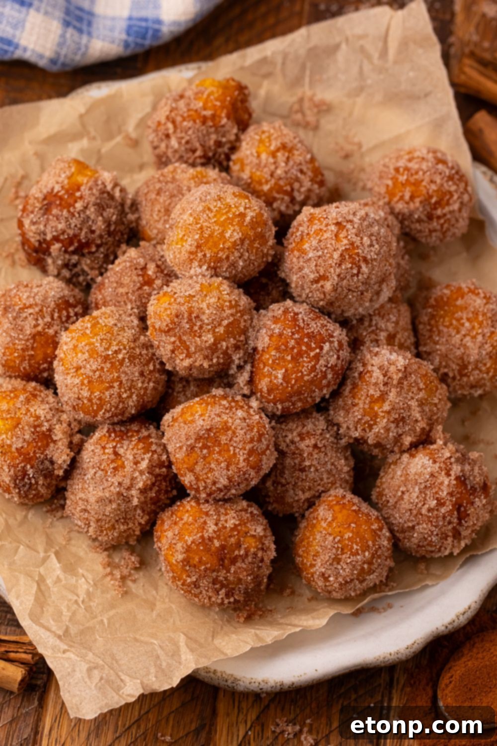 Effortless Two-Ingredient Pumpkin Pie Bites 16 Wooden table with a white platter full of a stack of Pumpkin Pie Donut Holes that are rolled in cinnamon and sugar