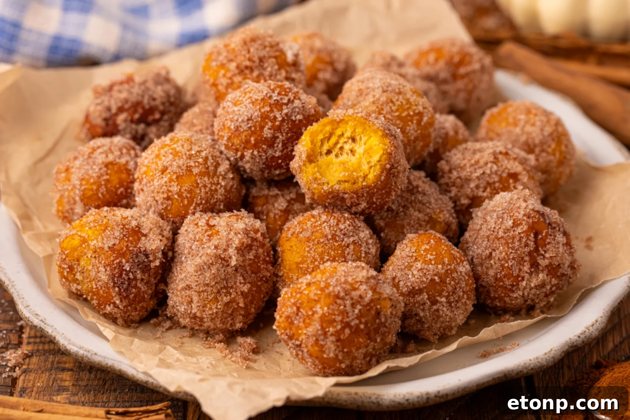 Effortless Two-Ingredient Pumpkin Pie Bites 17 Pumpkin Pie Donut Holes scattered on a parchment lined white platter on a wooden table.