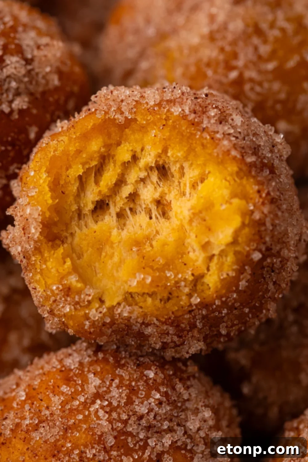 Effortless Two-Ingredient Pumpkin Pie Bites 18 Pumpkin Pie Donut Hole with a bite taken out of it, sitting on a pile of more of the donut holes