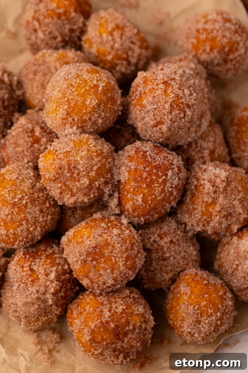 Effortless Two-Ingredient Pumpkin Pie Bites 19 a stack of Pumpkin Pie Donut Holes rolled in cinnamon and sugar coating with parchment paper under the donut holes