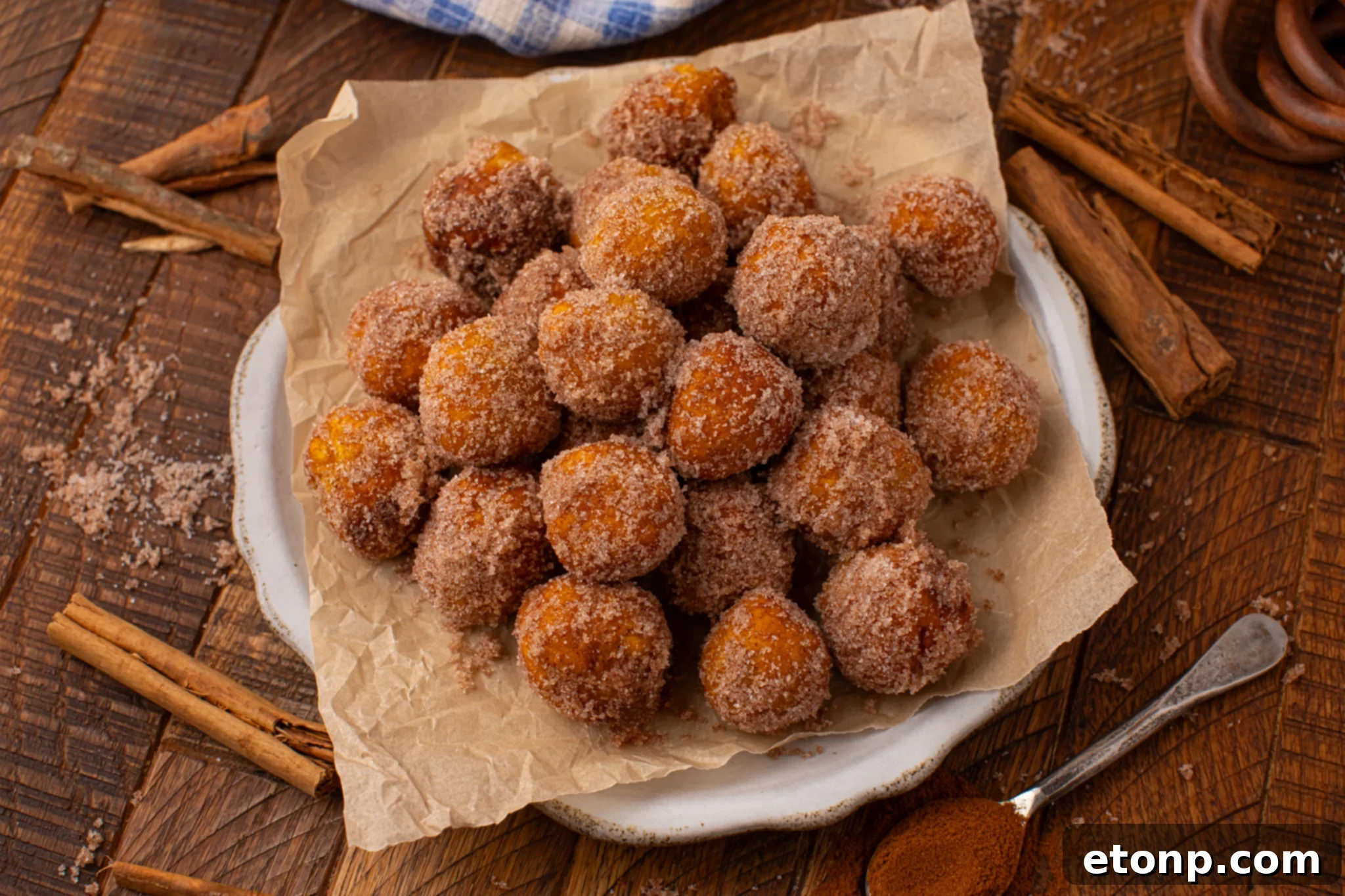 Effortless Two-Ingredient Pumpkin Pie Bites 20 overhead shot of the Pumpkin Pie Donut Holes scattered on a parchment lined white platter on a dark wooden table.