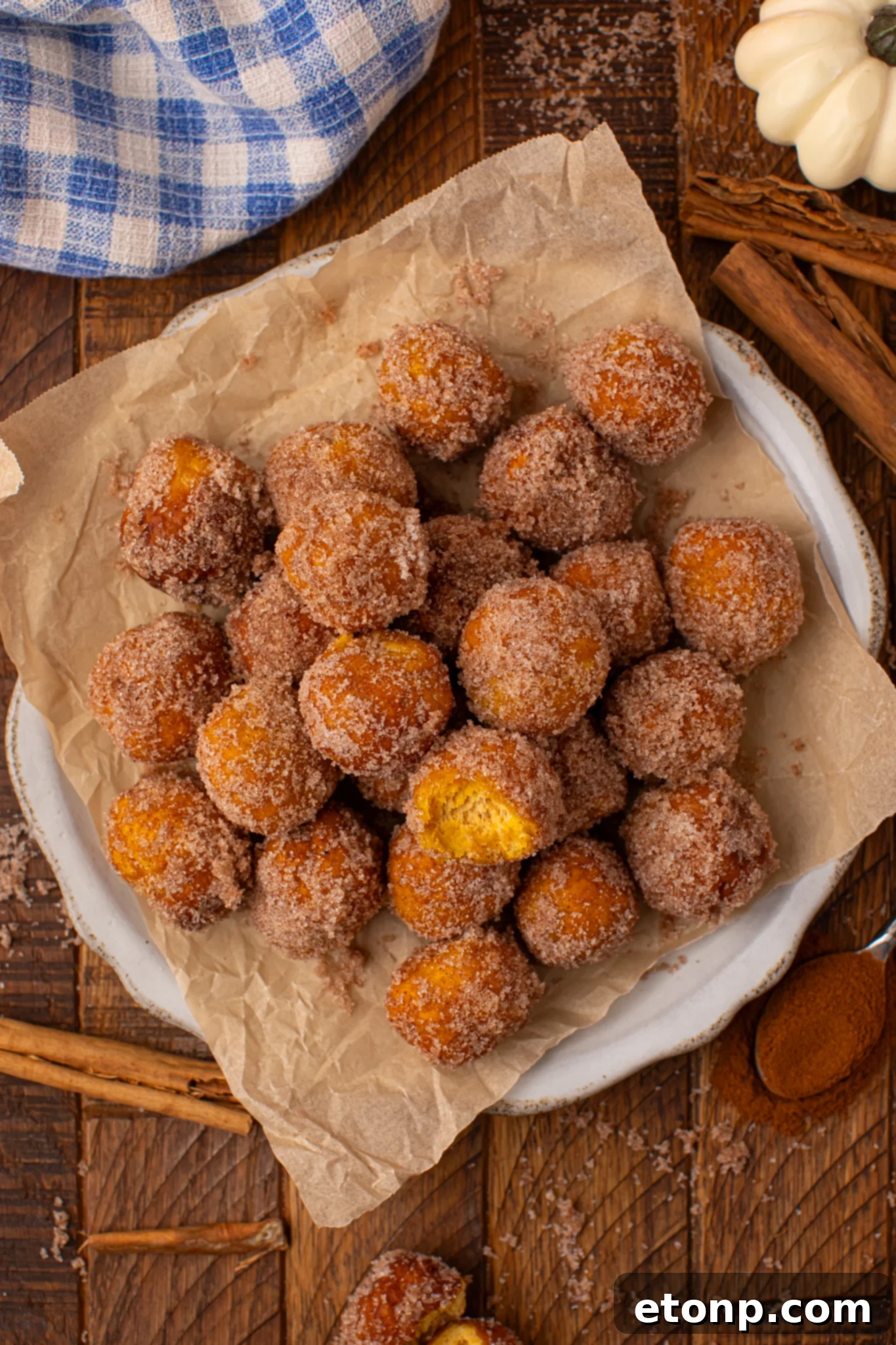 Effortless Two-Ingredient Pumpkin Pie Bites 23 Up close overhead shot oif the Pumpkin Pie Donut Holes scattered on a parchment lined white platter on a wooden table. The top donut hole has a bite taken out of it.