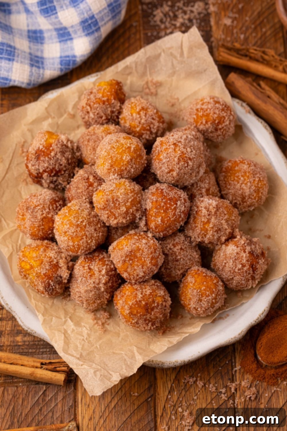 Effortless Two-Ingredient Pumpkin Pie Bites 4 Pumpkin Pie Donut Holes on a white plate with parchment paper under the donut holes with a blue checkered towel behind it