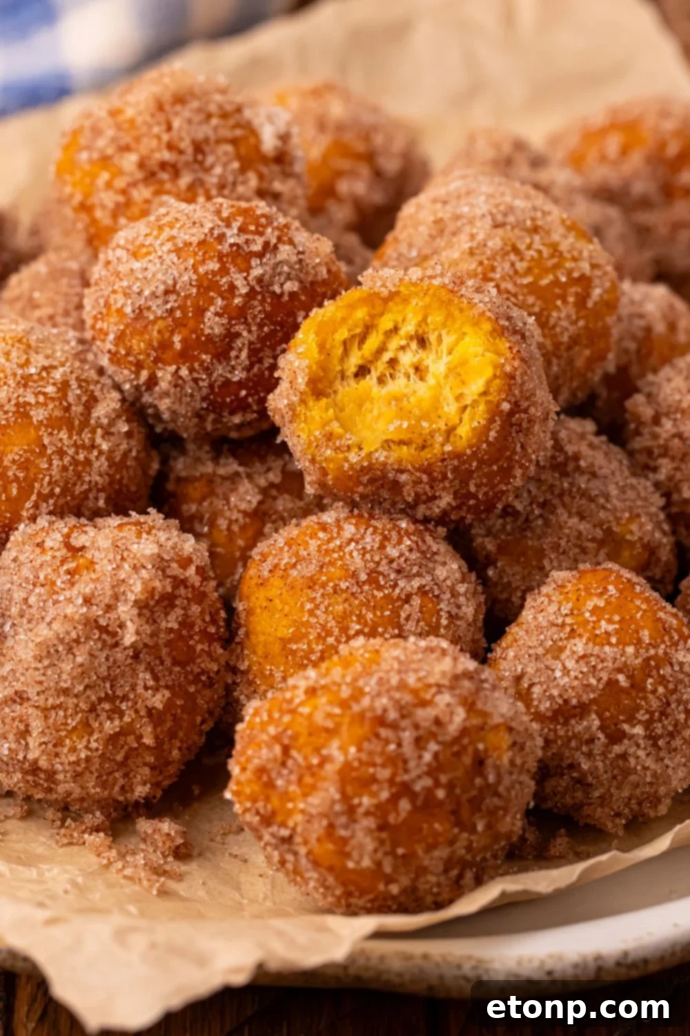 Effortless Two-Ingredient Pumpkin Pie Bites 10 donut holes rolled in cinnamon and sugar on a platter with one donut bit in half to show how fluffy it is