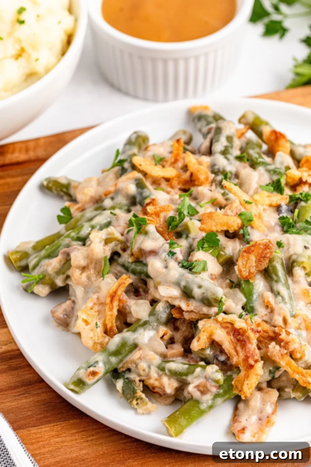 white plate sitting on table full of Green Bean Casserole. A brown towel is under the plate on table 