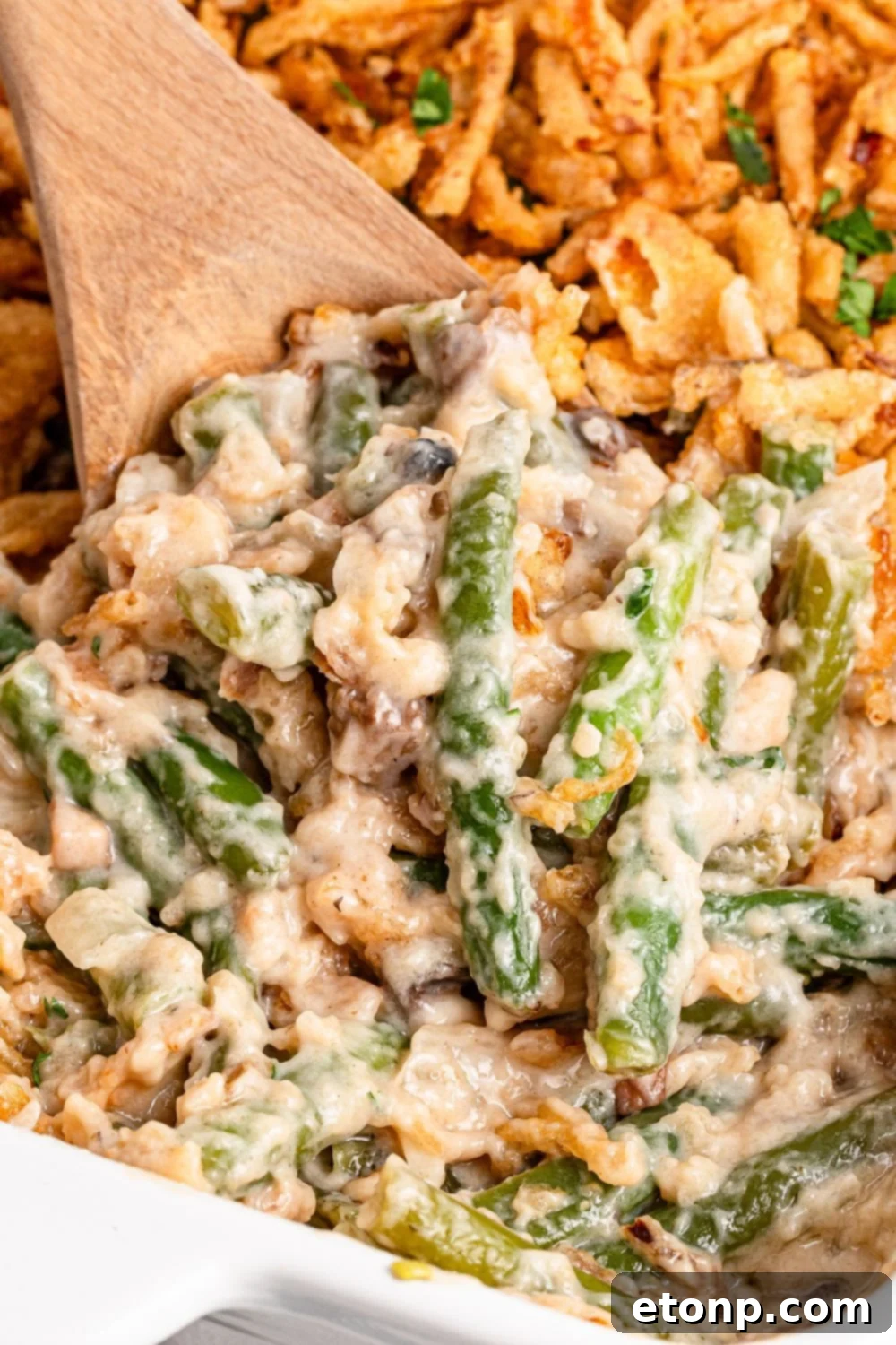 wooden spoon scooping up some of the Green Bean Casserole in a white baking dish on table 