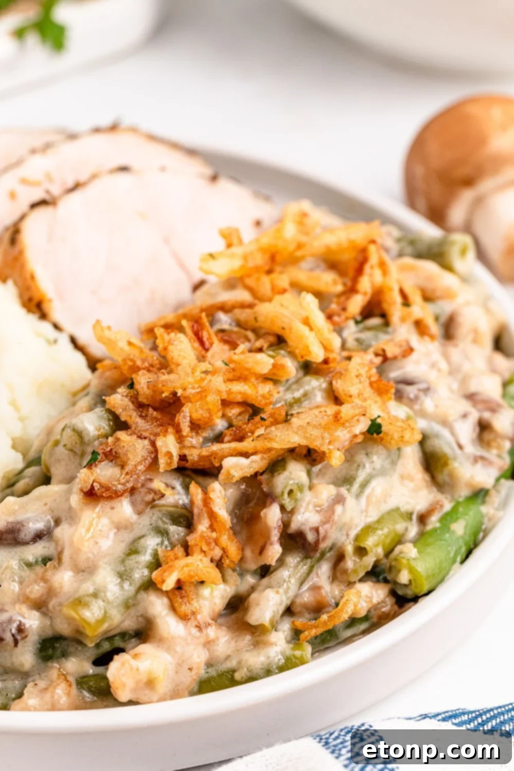 Green Bean Casserole on a round plate with some sliced turkey behind it on table and a striped towel in front of plate 