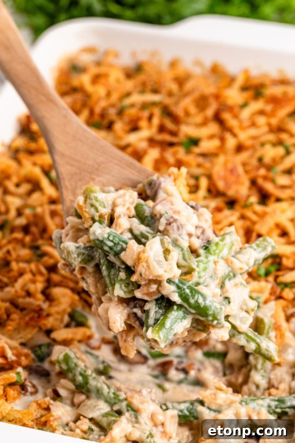 white rectangle pan on table full of Green Bean Casserole with a wooden spoon scooping some out of pan 