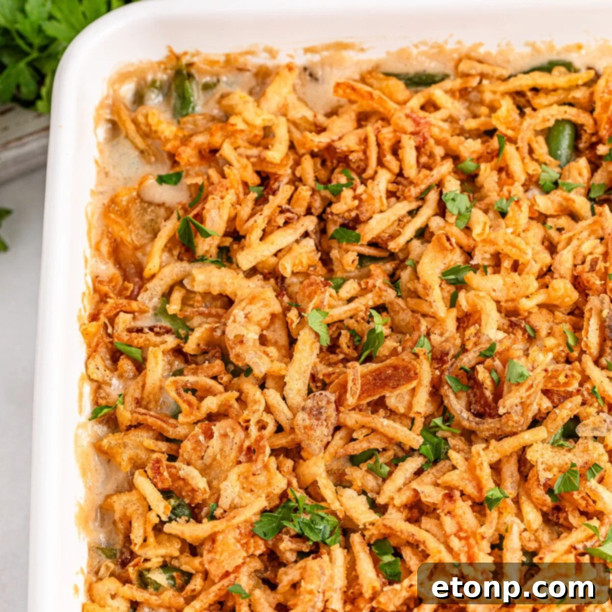 Green Bean Casserole in a white casserole  dish sitting on table with fresh parsley sprinkled on top of casserole 