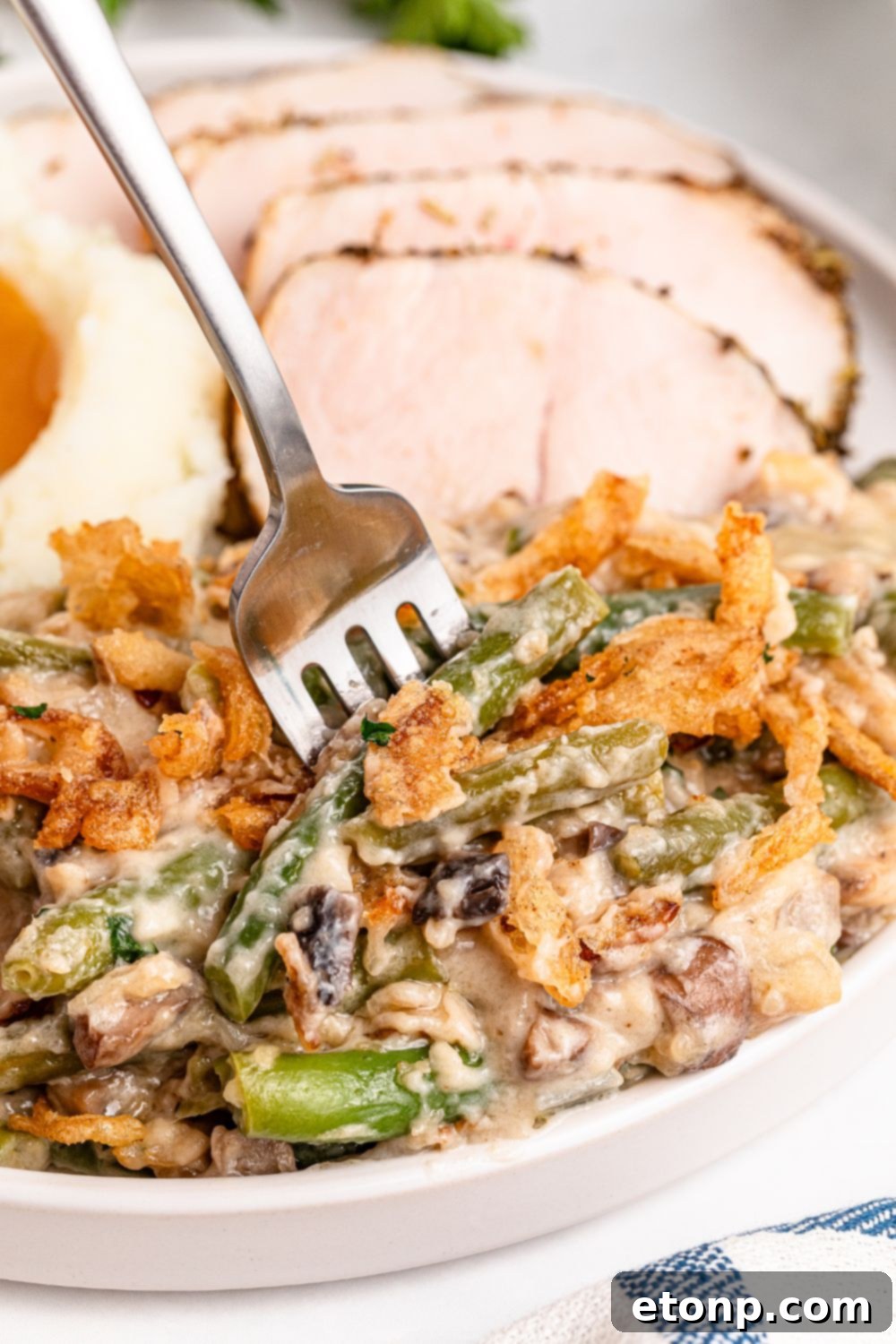 forking poking into plate full of Green Bean Casserole, with sliced turkey breast behind it and a bit of mashed potatoes and gravy