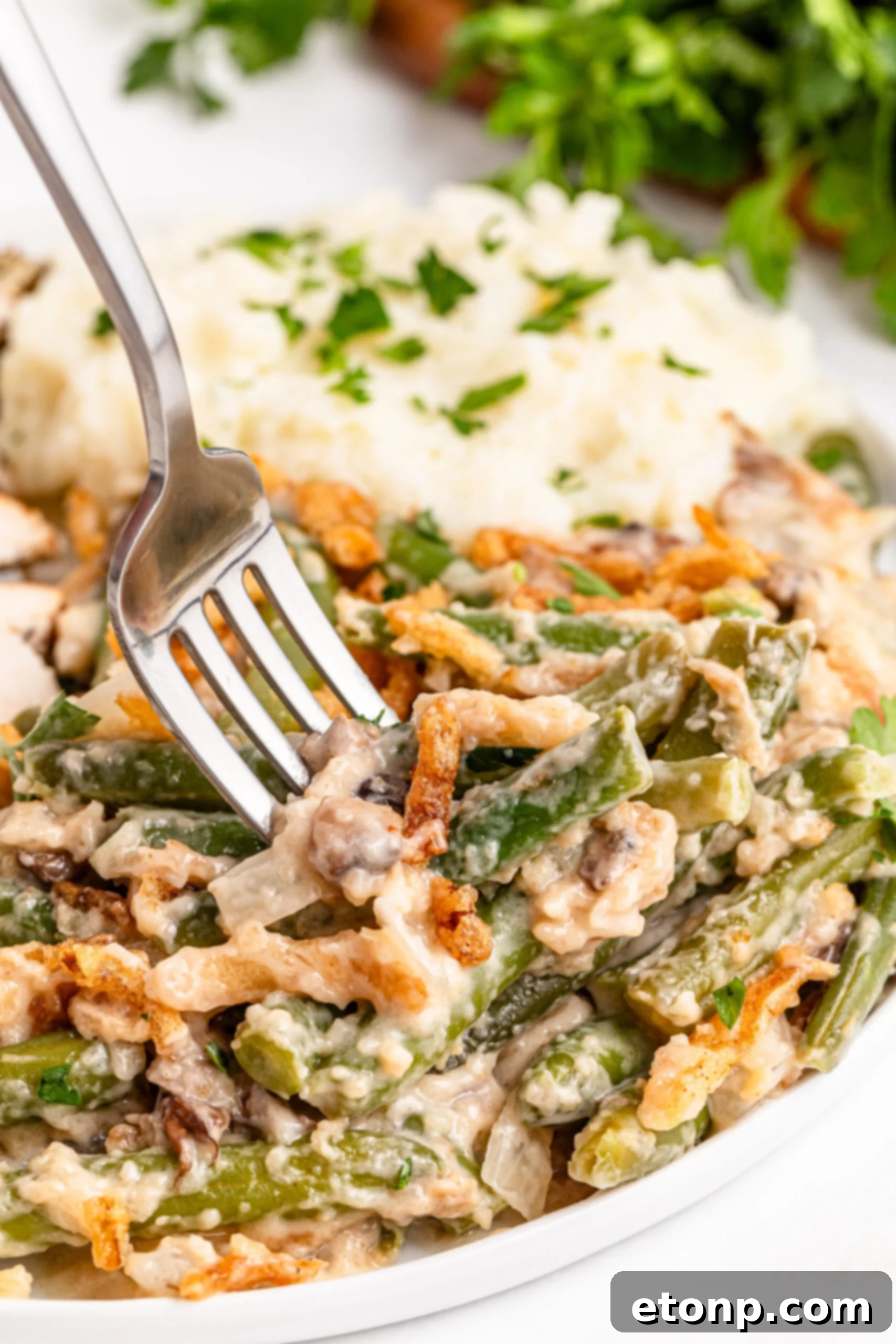 a fork going in for a bite of the Best Ever Green Bean Casserole in a white plate