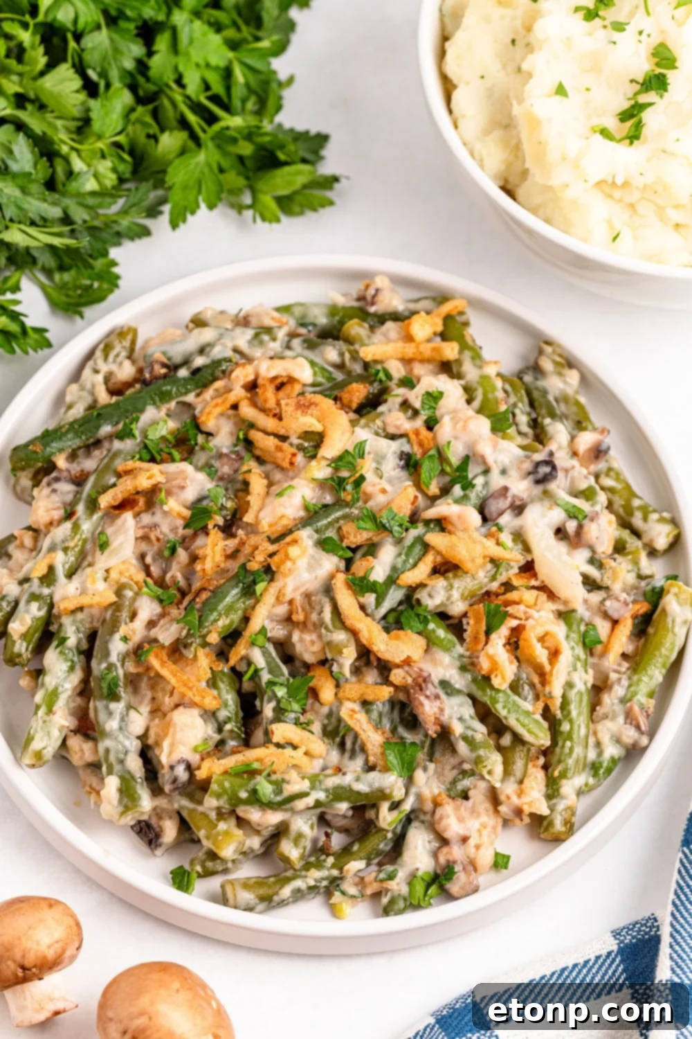 round white plate full of Green Bean Casserole with some fresh mushrooms to side on table, and fresh parsley