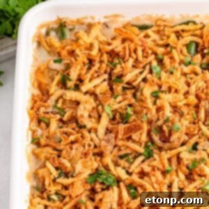 Green Bean Casserole in a white casserole dish sitting on table with fresh parsley sprinkled on top of casserole