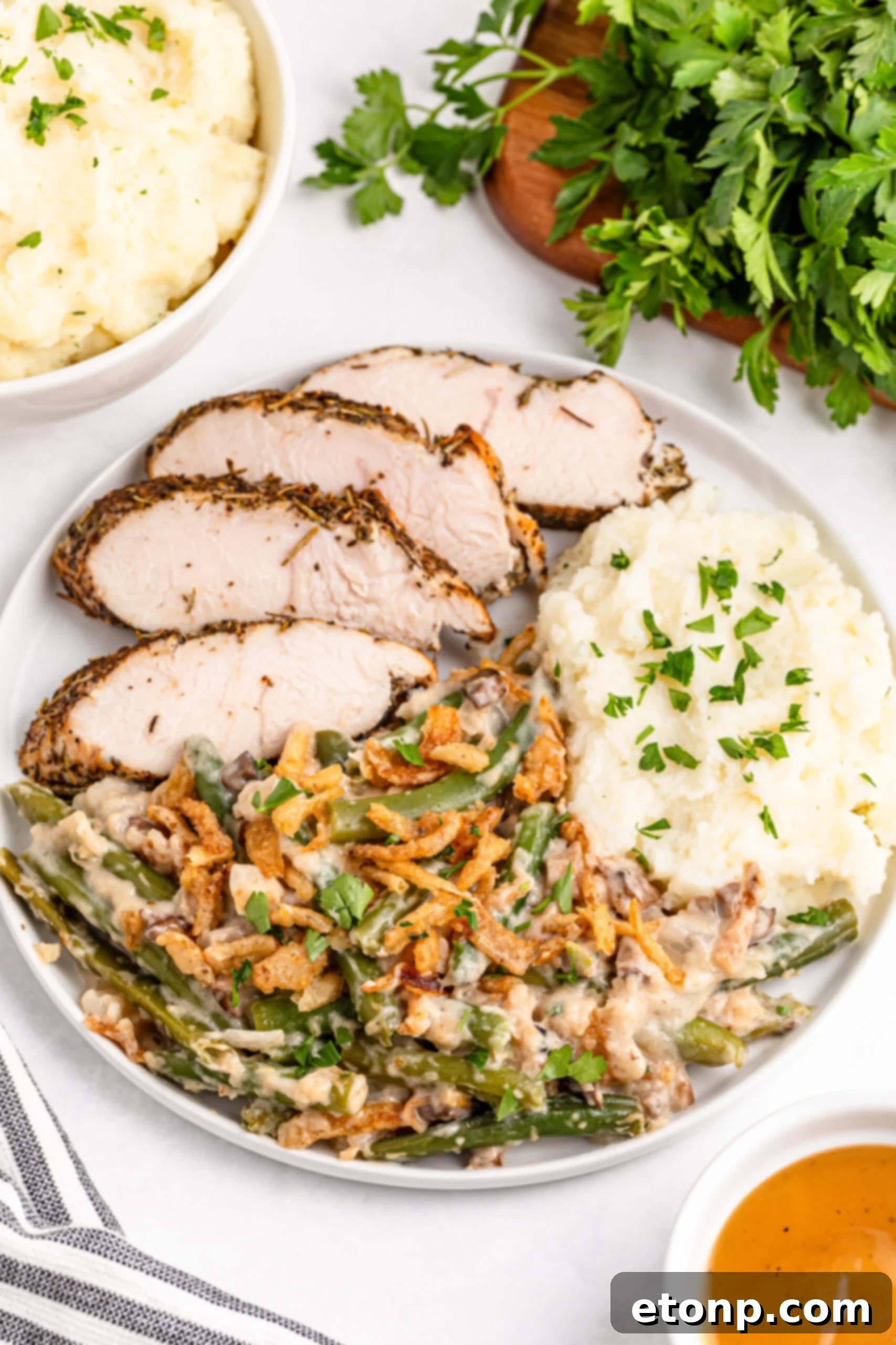 Green bean casserole on a white plate along side mashed potatoes and sliced turkey 