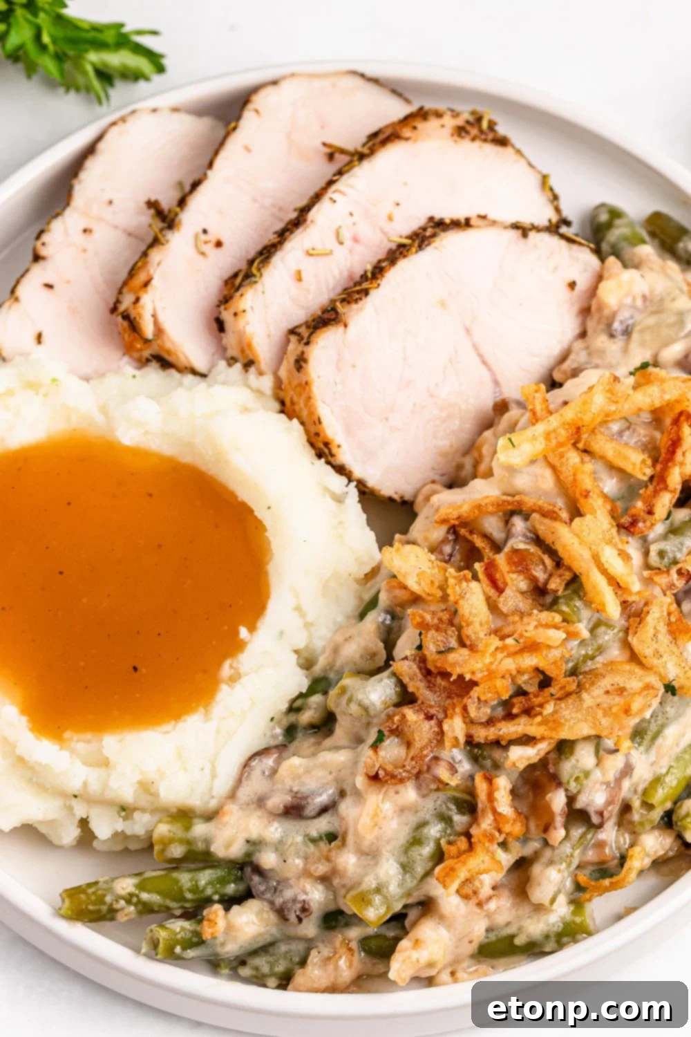 a white plate on a table with slices of turkey, scoop of mashed potatoes and gravy and some green bean casserole on it 