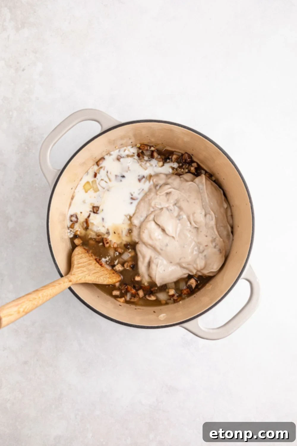cream colored saucepan on table full of cooked veggies, cream soup and milk with wooden spoon 