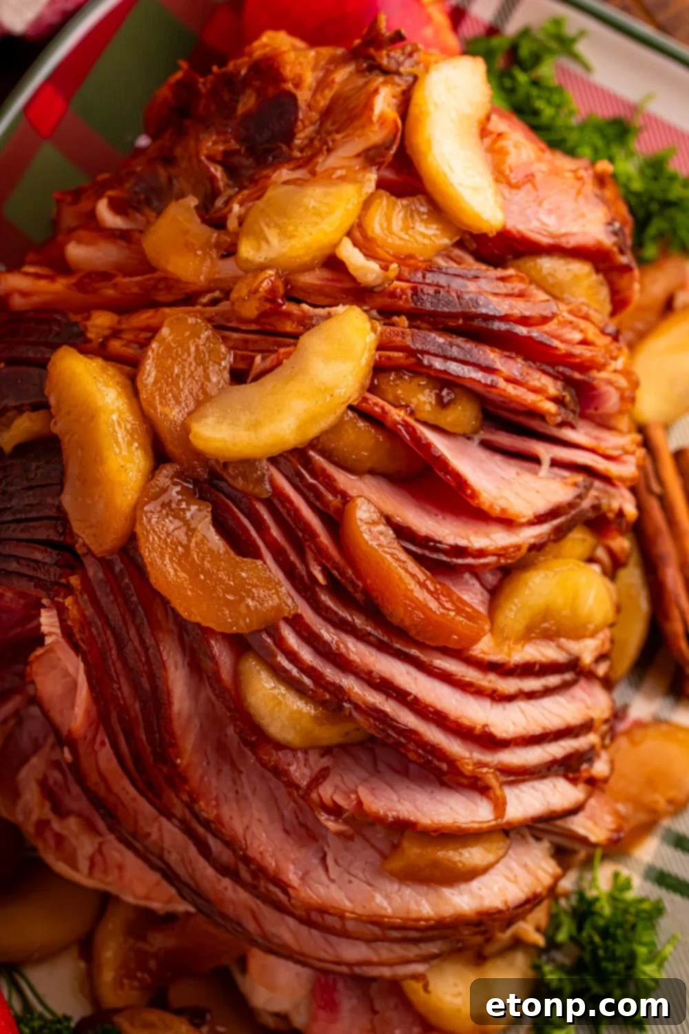fully cooked Slow Cooker Apple Glazed Ham on a platter garnished with greens and cinnamon apples on top of ham 
