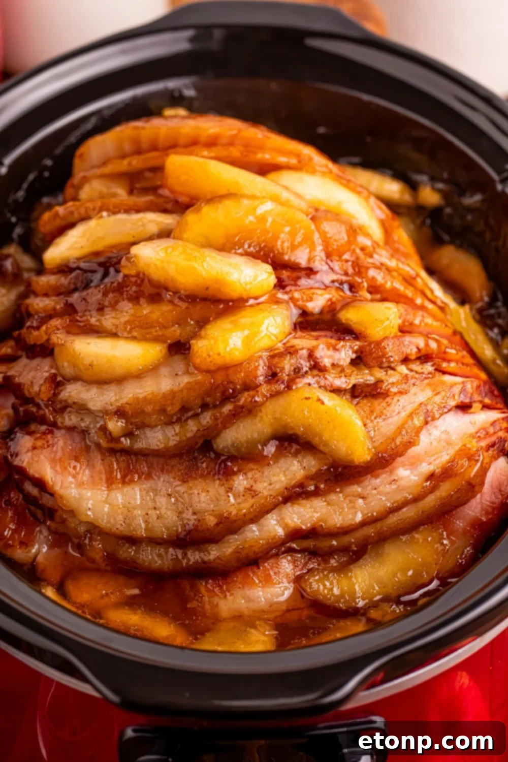 red slow cooker on table with a glazed apple spiral ham on table 