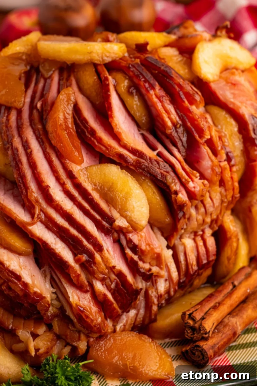 side view of a Slow Cooker Apple Glazed Ham sitting on a platter with cinnamon sticks in front 