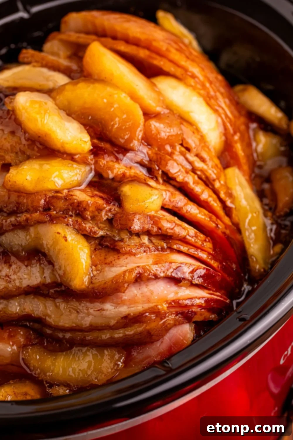 close up look of a red slow cooker with a apple topped spiral ham