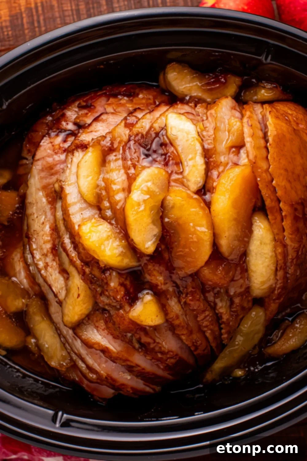 looking down at a black slow cooker with a spiral cut ham and baked apples on top of the ham