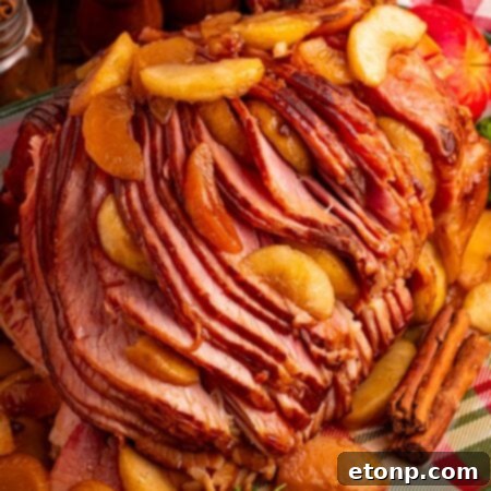 Slow Cooker Apple Glazed Ham on a plaid platter sitting on table with a checkered red towel behind ham, salt and pepper shakers