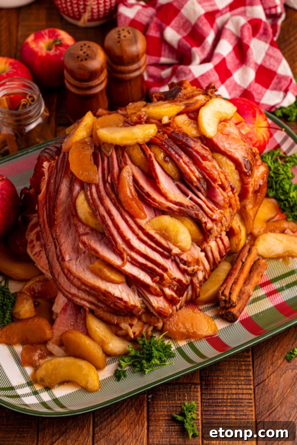 A plaid platter on a wooden table with a large Slow Cooker Apple Glazed Ham on platter, and fall themed items around it