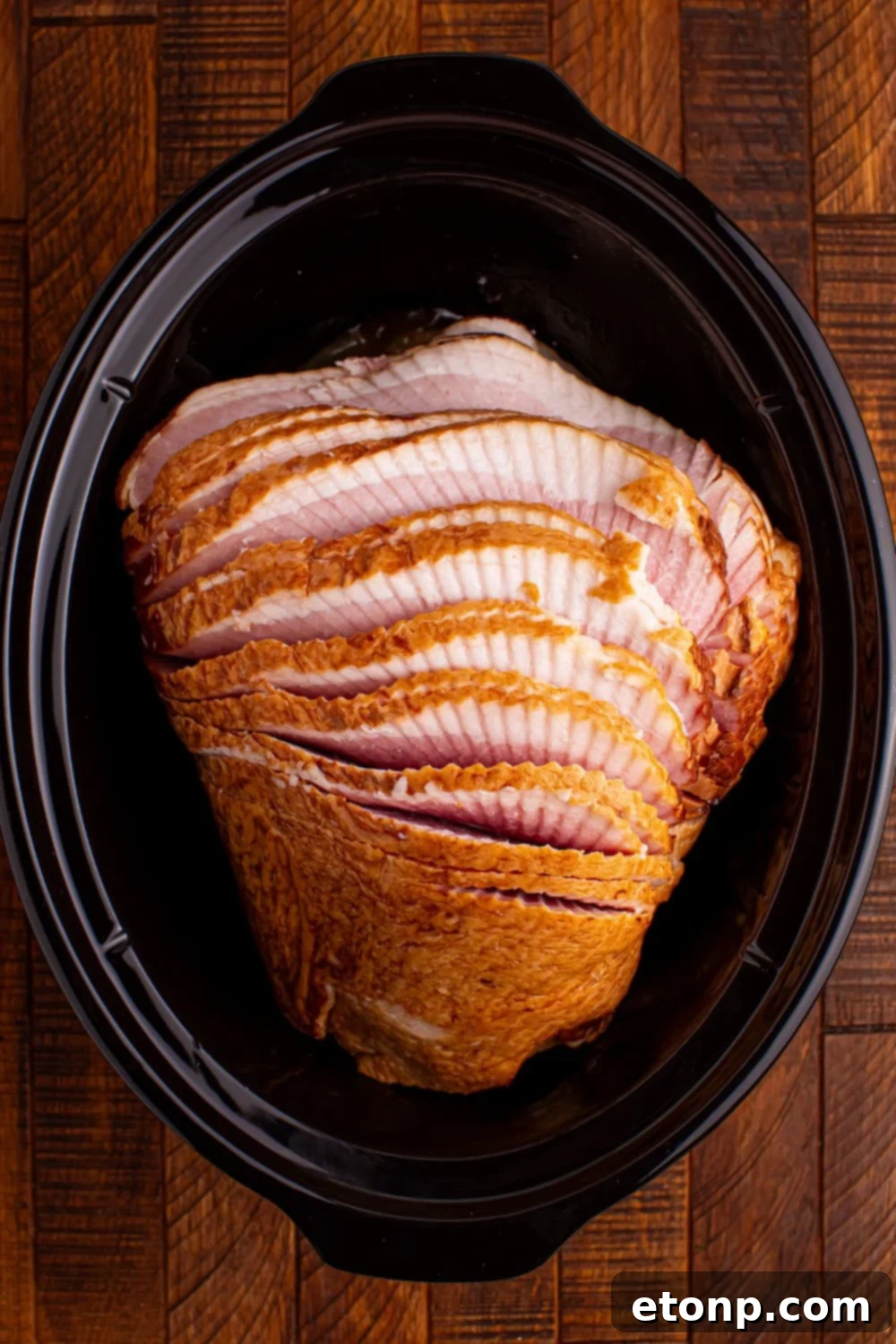 raw spiral cut ham sitting on a wooden table in a black slow cooker