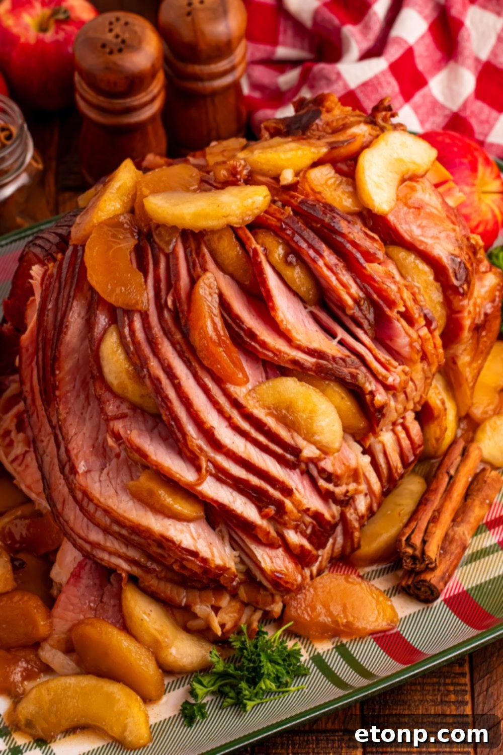 Slow Cooker Apple Glazed Ham on a plaid platter sitting on table with a checkered red towel behind ham, salt and pepper shakers 