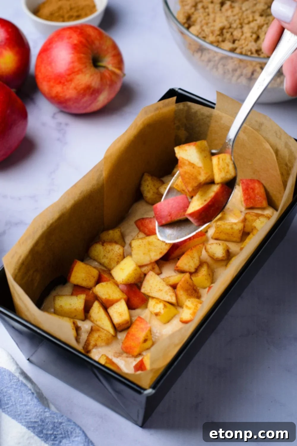 cinnamon cubed apples being put into the loaf pan on top of batter for making Apple Cinnamon Loaf Cake