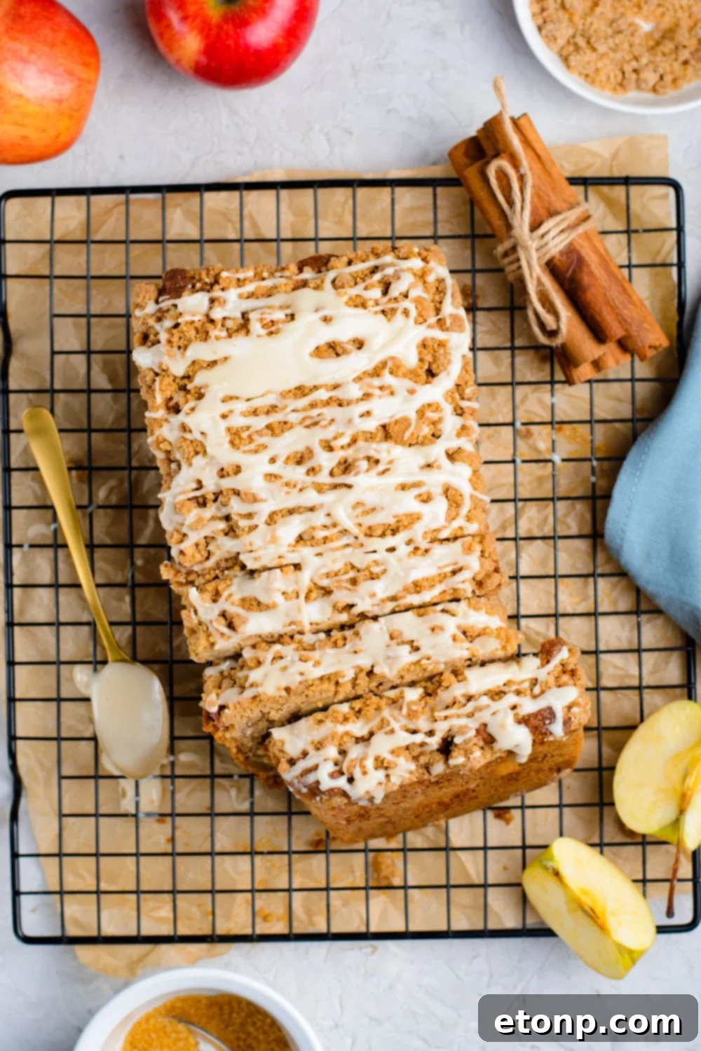 Apple Cinnamon Loaf Cake on a cooling rack on marble counter with a bundle of cinnamon sticks to the side, apples, sliced apples and more to decorate it for fall
