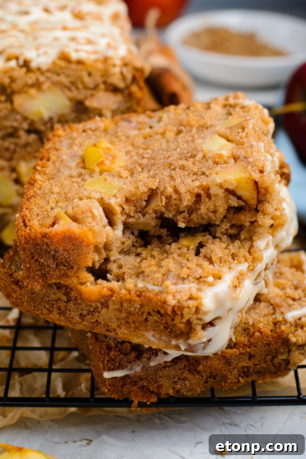 3 slices of Apple Cinnamon Loaf Cake on top of one another sitting on a wire cooling rack on table with the top slice having a few bites taken out of it