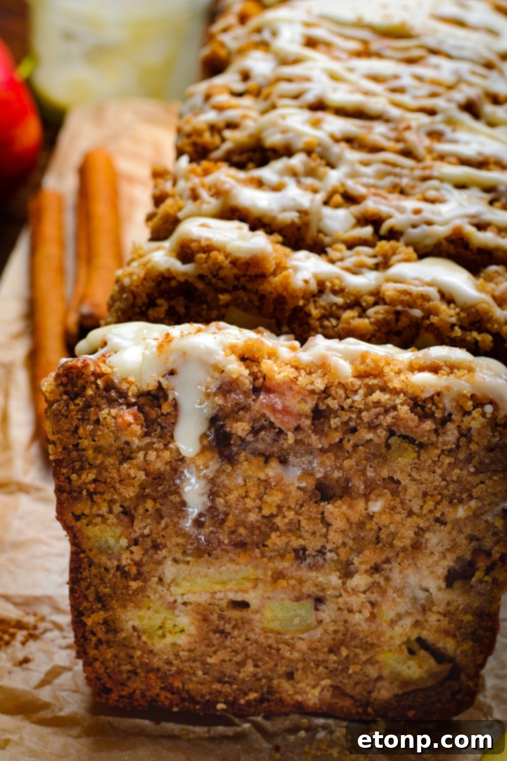 side view of the apple loaf cake on table with a sweet drizzle on top and two cinnamon sticks to the side on wooden table