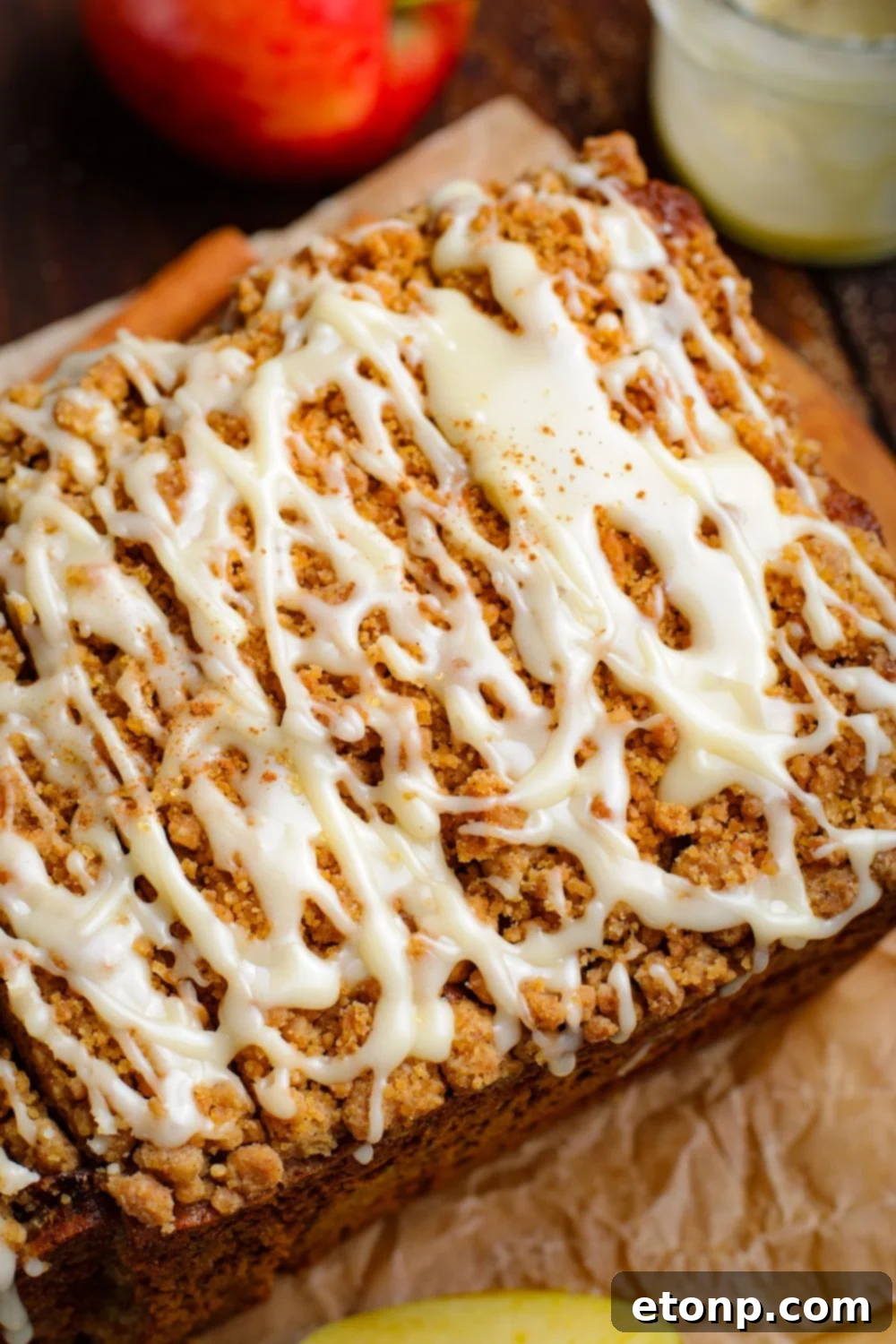Apple Cinnamon Loaf Cake on parchment paper on a wooden table with a glass of glaze to side and red apple