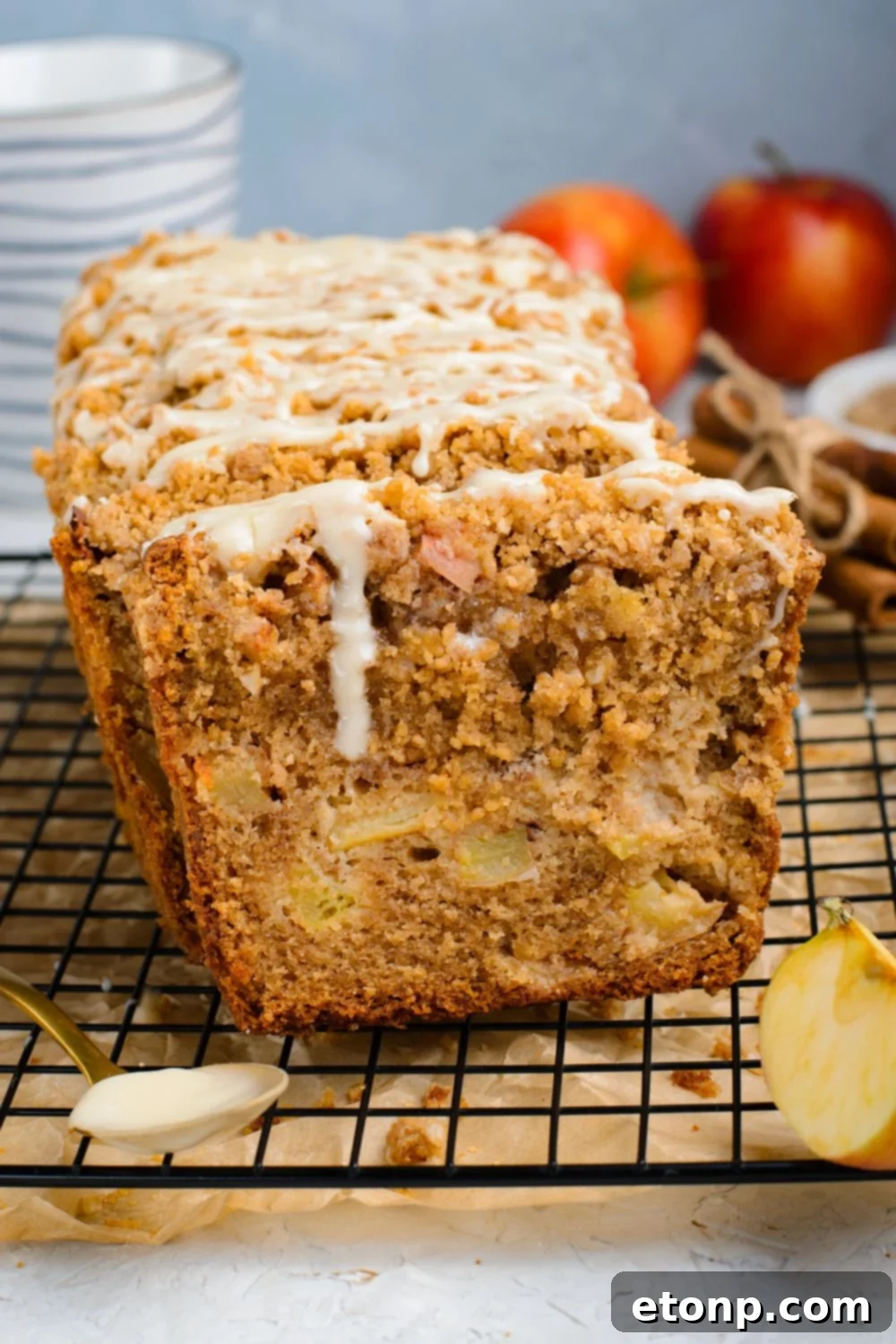 metal cooling rack with parchment paper under it sitting on table with a loaf of Apple Cinnamon Loaf Cake sliced and topped with a white glaze