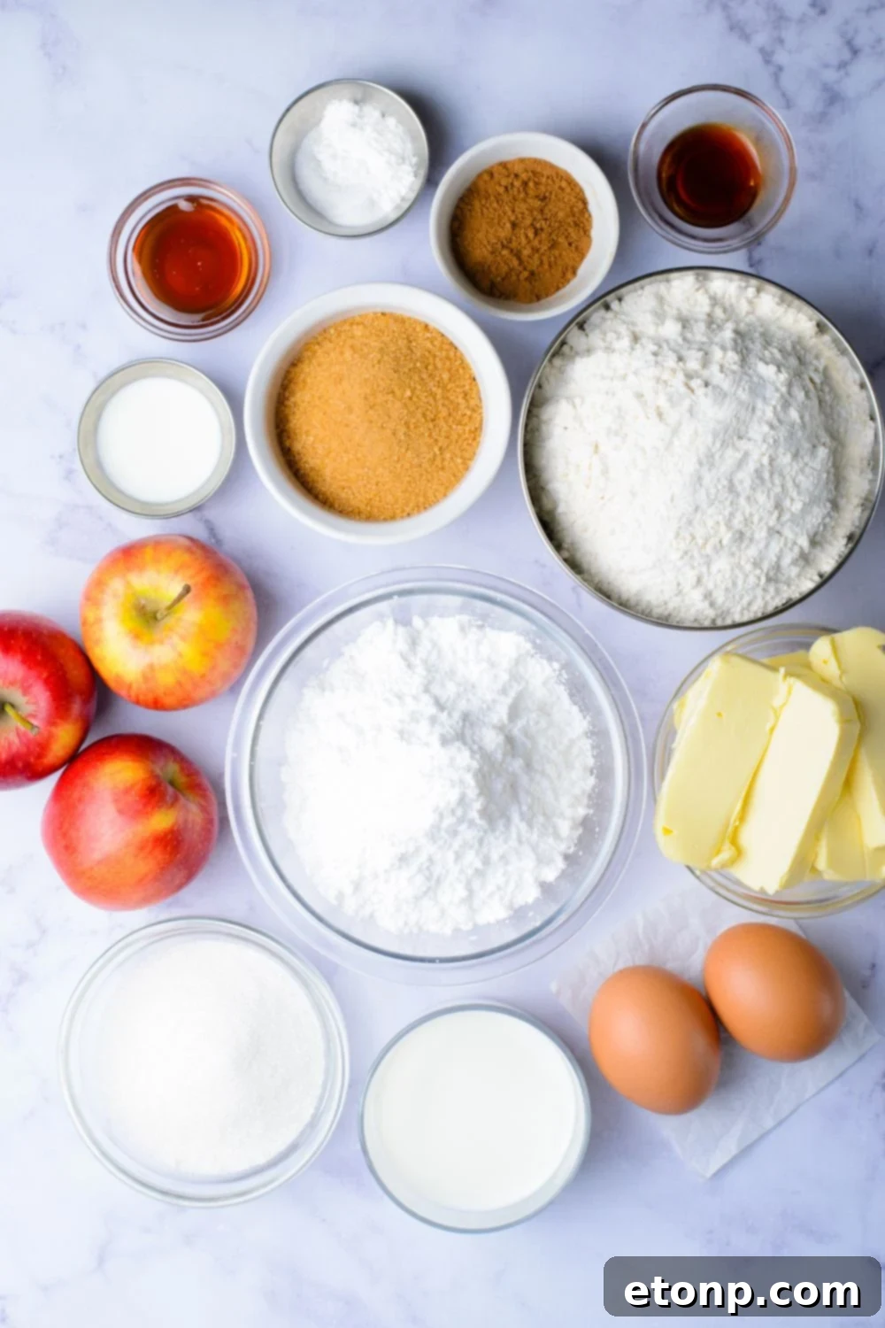 all the ingredients for Apple Cinnamon Loaf Cake in single serve small glass bowls on marble counter and whole apples and eggs included
