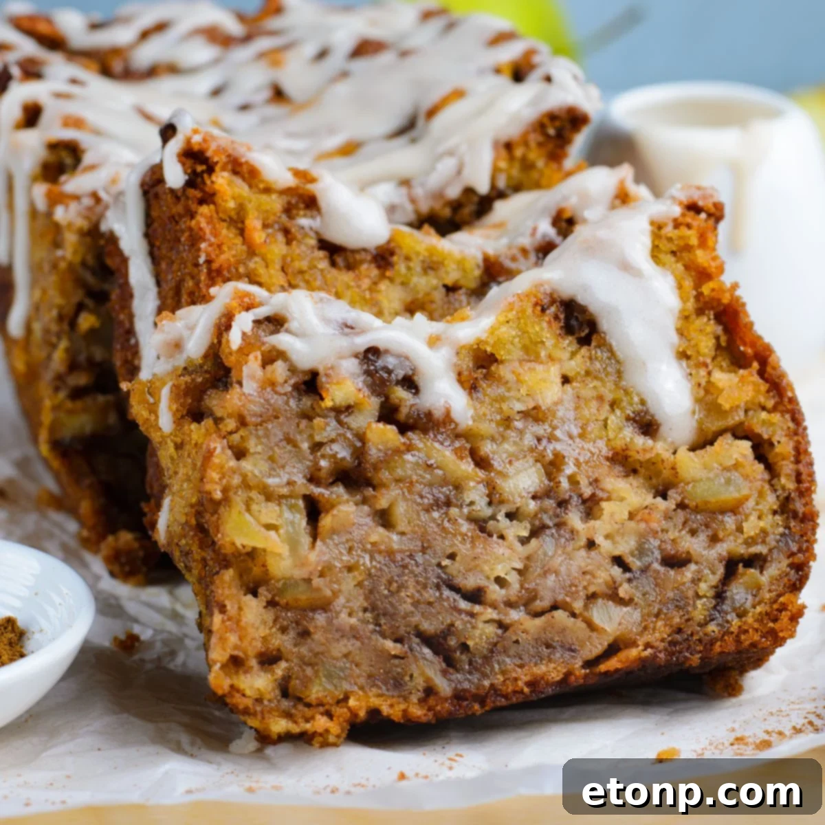 Amish Apple Fritter Bread sliced and placed on a parchment paper on table with a bowl with glaze to the side