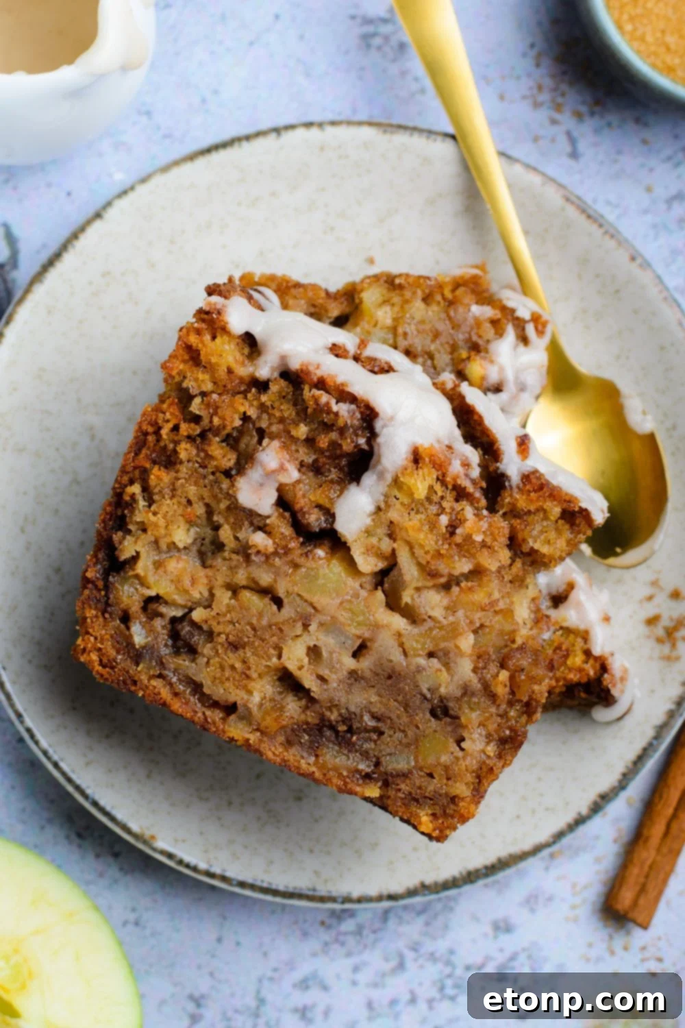 two slices of Amish Apple Fritter Bread on plate with a spoon to side of plate with a few bites taken out sitting on blue table