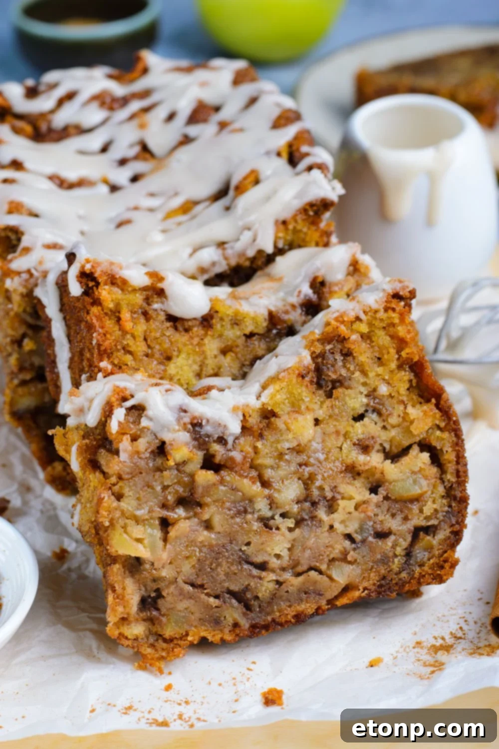 sliced Amish Apple Fritter Bread sitting on parchment paper on a wooden table with a sweet glaze drizzled on top