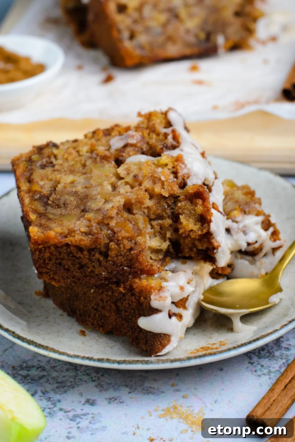 two slices of Amish Apple Fritter Bread on a white plate with a gold spoon to side showing a couple bites taken out of it