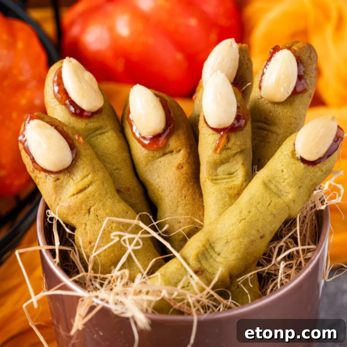 Witch Finger Cookies in a basket with straw in it with pumpkins and leaves on the table behind it 