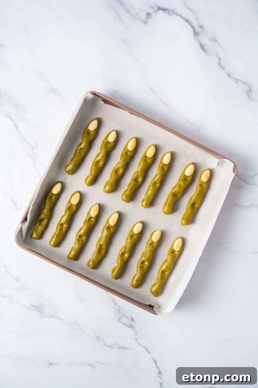 raw pistachio Witch Finger Cookies on a parchment paper lined tray with almonds for finger nails
