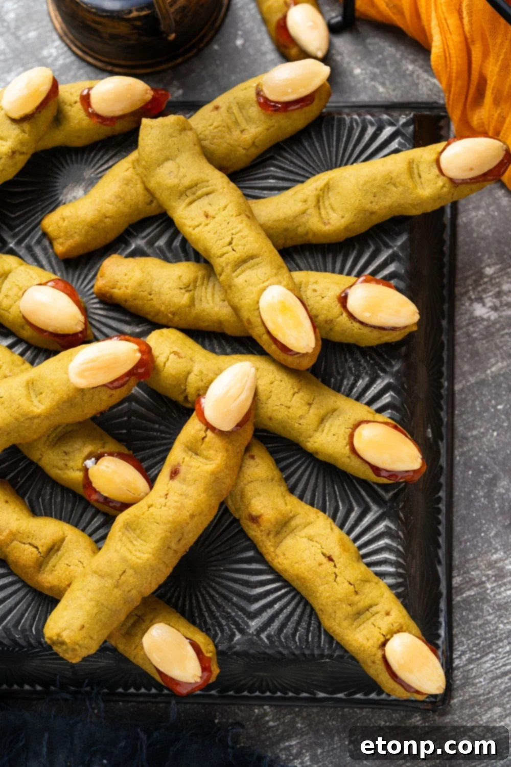 black tray with Witch Finger Cookies scattered on it with some Halloween decor on the table around the tray 